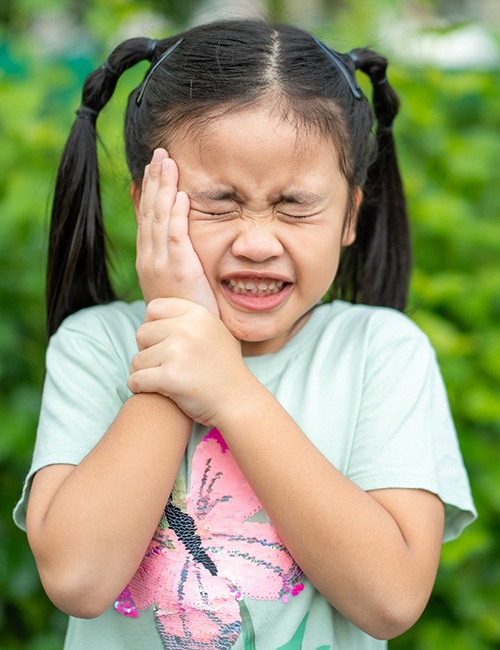Little girl with pigtails squinting eyes and holding hand to cheek in pain